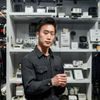 国产自拍研究院配件测评人赵明宇，男性，手持多款自拍配件展示，背景为整齐的摄影器材陈列架
